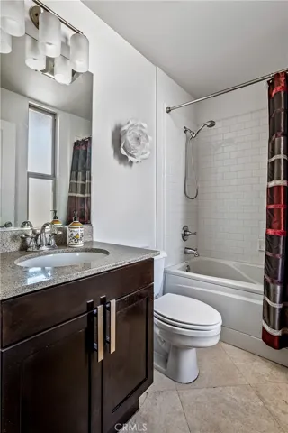 Full secondary bathroom with stone countertop, dark wood vanity, and tiled tub-and-shower enclosure.