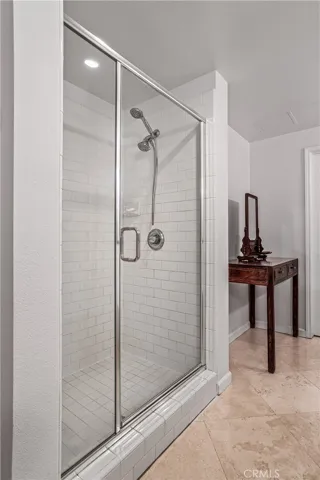 Separate glass enclosed shower with clean white tile and handheld shower fixture.