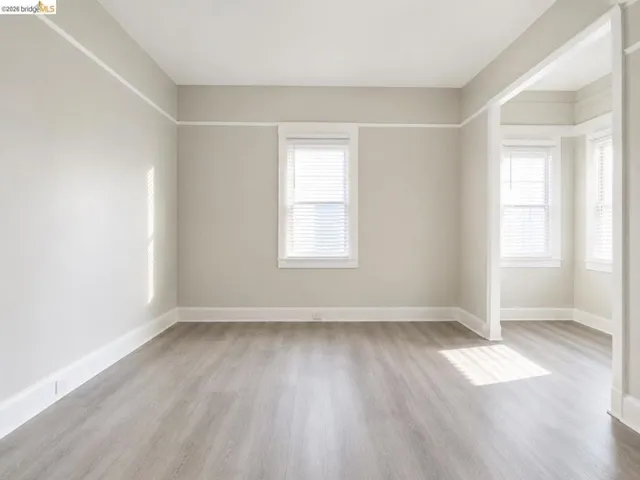 Spacious interior featuring wood-finish flooring, neutral wall tones, white trim, multiple windows with blinds, and an open entryway