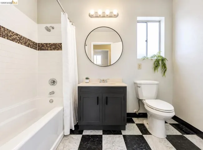 Bathroom featuring a white bathtub and shower with mosaic tile accent, black and white checkerboard flooring, dark wood-finish vanity with countertop, and an overhead vanity light fixture