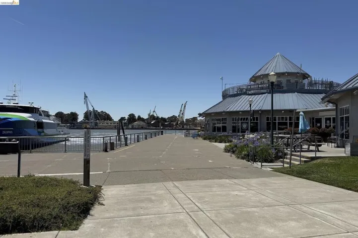 Waterfront promenade featuring a modern building with a circular roof, outdoor seating, and a ferry terminal