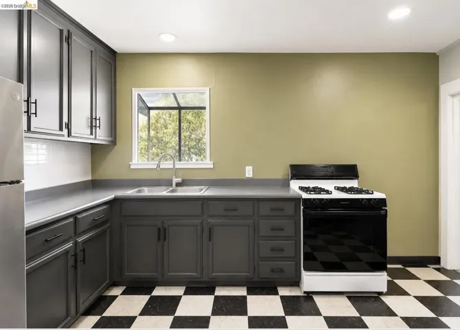 Kitchen featuring dark gray cabinetry, matte black hardware, dual basin stainless steel sink, white subway tile backsplash, and checkerboard floor tiling