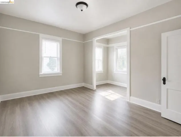 Spacious room featuring wood-finish flooring, neutral paint palette, crisp white trim, multiple windows with blinds, and an overhead flush-mount light fixture