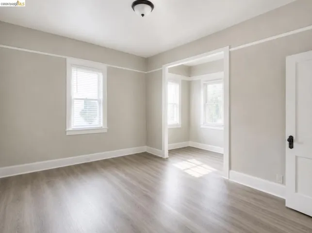 Neutral tone walls with white trim, wood-finish flooring, two windows with blinds, and a traditional ceiling light fixture