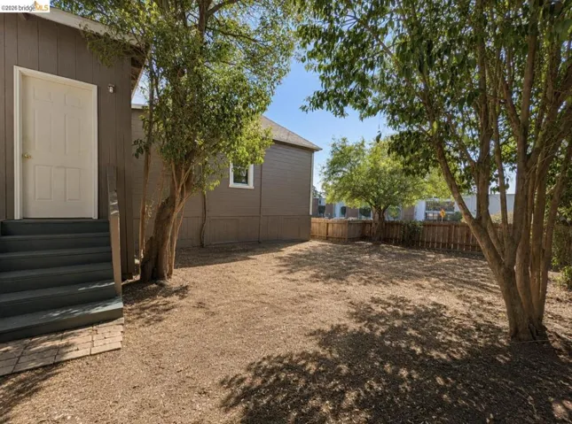 Spacious rear yard featuring natural ground cover and mature trees, surrounded by a wood privacy fence
