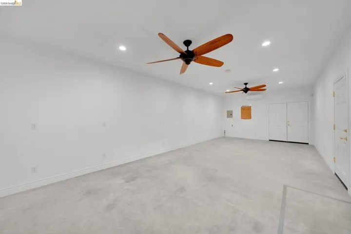 Spacious room with light-toned flooring, featuring a pair of ceiling fans with wood-finish blades, recessed lighting, and white walls
