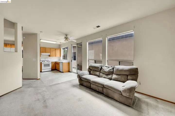 Carpeted living area with abundant natural light from three windows and an adjacent kitchen