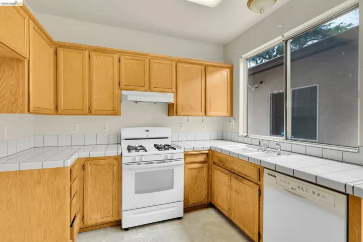 Kitchen featuring light wood cabinetry, white tile countertops, a white gas range, and a dual basin sink