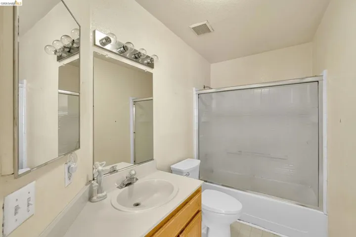 Bathroom featuring a vanity with a white countertop and integrated sink, a large wall-mounted mirror, and a chrome light fixture with exposed bulbs