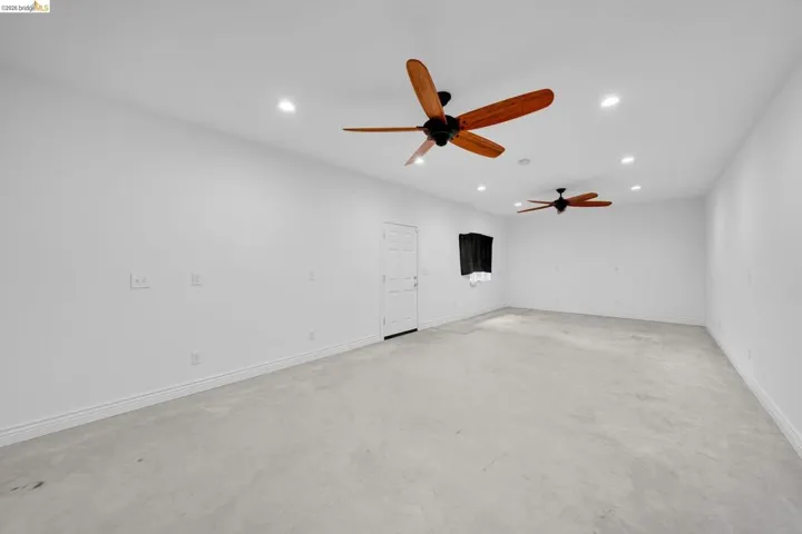Spacious room featuring light gray flooring, white walls, two ceiling fans with wood-finish blades, recessed lighting, and a white interior door