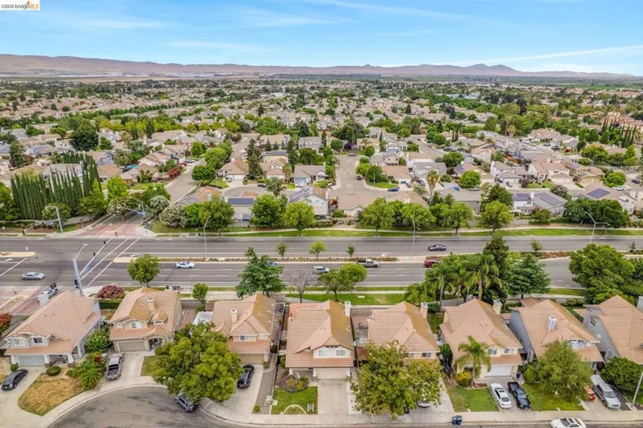 Residential neighborhood featuring mature trees, a multi-lane thoroughfare, and distant mountains