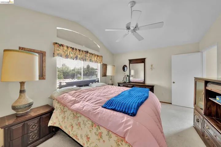 Vaulted ceiling room featuring a ceiling fan, arched window, and carpet flooring