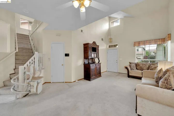 Spacious living area featuring high ceilings, carpet flooring, a front entry door with transom window, and a staircase with a chair lift