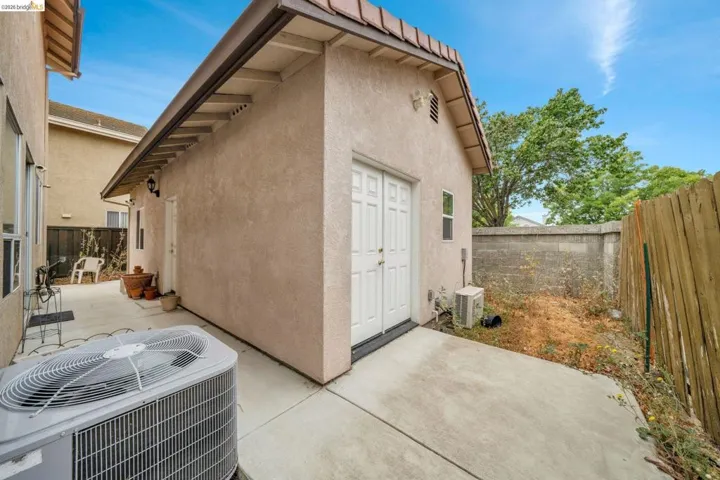 Detached stucco structure featuring double doors and a window, concrete patio, and a concrete block wall