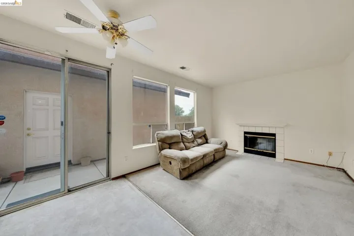 Living area featuring a ceiling fan with integrated lighting, a fireplace with a white tile surround, and two windows