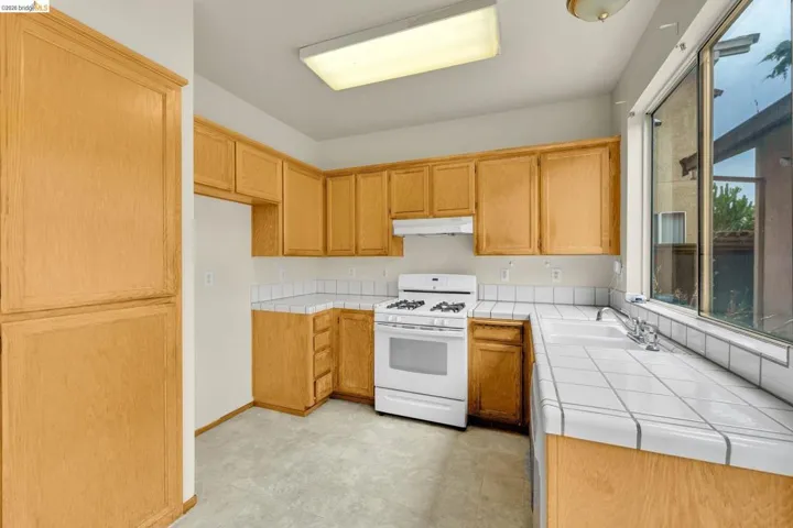 Full kitchen featuring wood-finish cabinetry, white tile countertops, and a white gas range with coordinating​​‌​​​​‌​​‌‌​​‌​​​‌‌​​​‌​​‌‌​​‌‌​​‌‌​​​​ hood