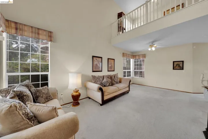 Spacious living area featuring a vaulted ceiling, an upper-level balcony with white railings, and light-colored wall paint
