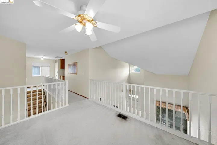 Carpeted loft area featuring a ceiling fan with integrated lighting, white baluster railing, and a sloped ceiling detail