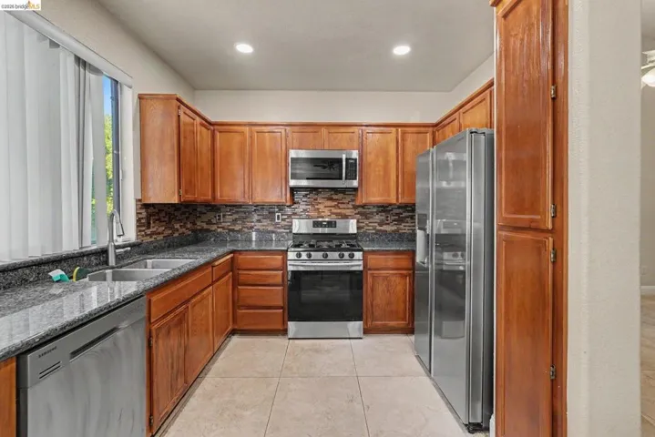 U-shaped kitchen featuring wood cabinetry, stainless steel appliances, dark speckled countertops, and a mosaic tile backsplash