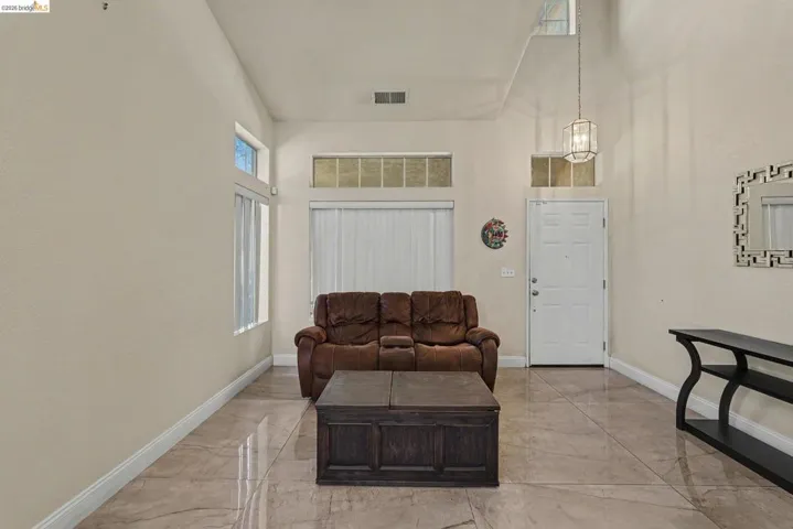 Spacious living area featuring vaulted ceilings, light-toned wall finishes, large format tile flooring, and ample natural light from multiple windows