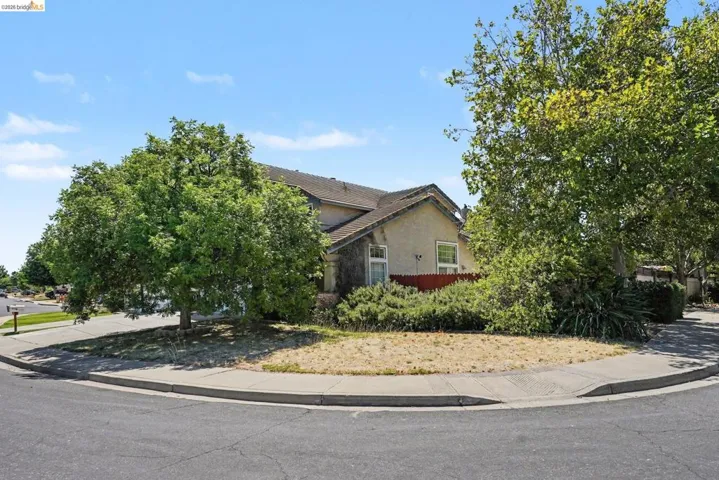 Corner lot property with a stucco exterior, multiple mature trees, and a red privacy fence