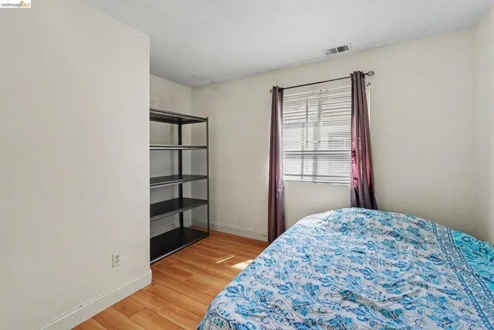 Room featuring wood-finish flooring, a window with blinds, and white baseboards