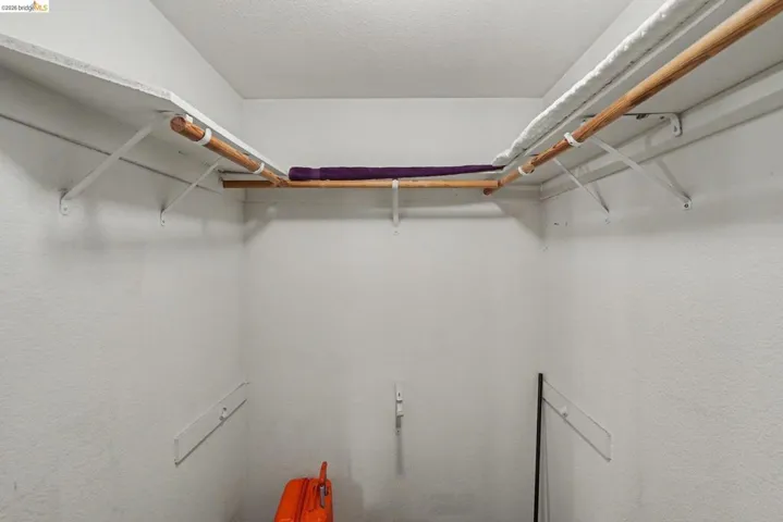 Walk-in closet featuring white walls, a white ceiling, and a built-in shelving system with hanging rods