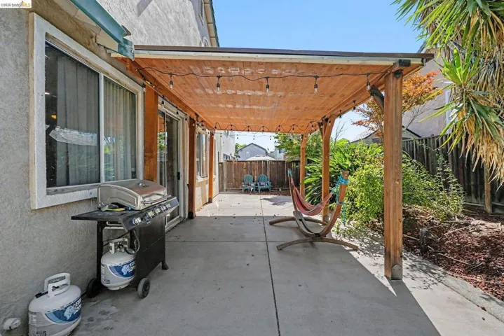 Outdoor patio featuring a wood pergola with string lighting, concrete flooring, and mature landscaping