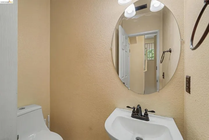 Pedestal sink with a dark bronze faucet, accompanied by an oval frameless mirror and a three-light vanity fixture