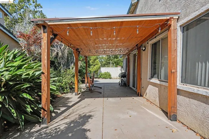 Expansive concrete patio featuring a wood pergola with integrated string lighting