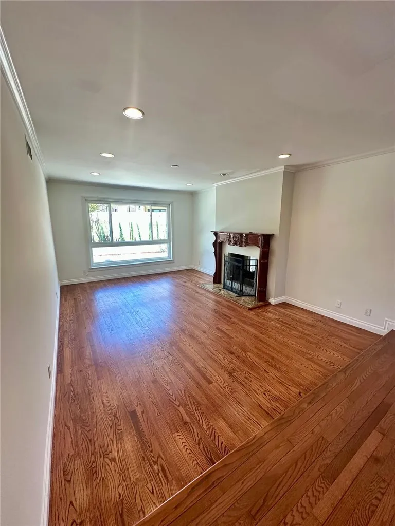 Spacious formal living room with recessed lights and huge window on the backyard side along with an elegant fireplace and mantle