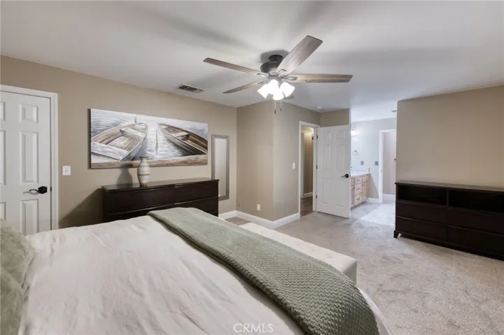 Expansive primary suite boasting neutral tones, plush carpeting, ceiling fan, and large windows bringing in natural light.