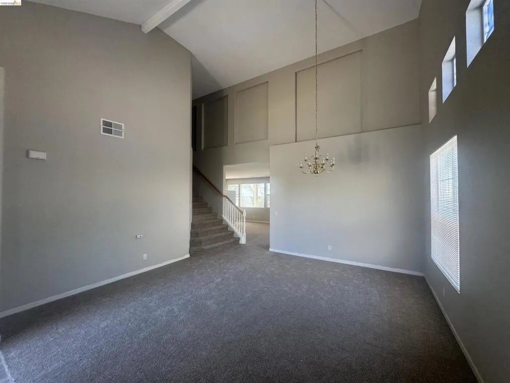 Unfurnished living room featuring beam ceiling, dark carpet, high vaulted ceiling, a chandelier, and stairway