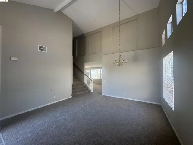 Unfurnished living room featuring beam ceiling, dark carpet, high vaulted ceiling, a chandelier, and stairway