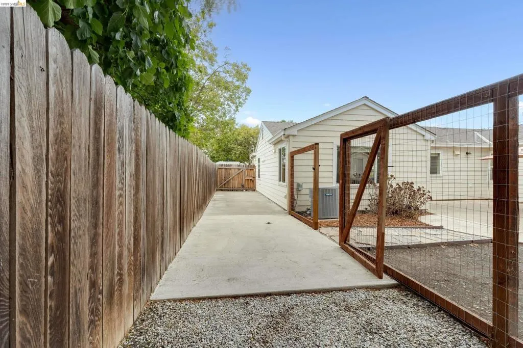 Concrete side yard with gravel bordering, wood privacy fencing, and a separate wood-framed wire fence enclosure