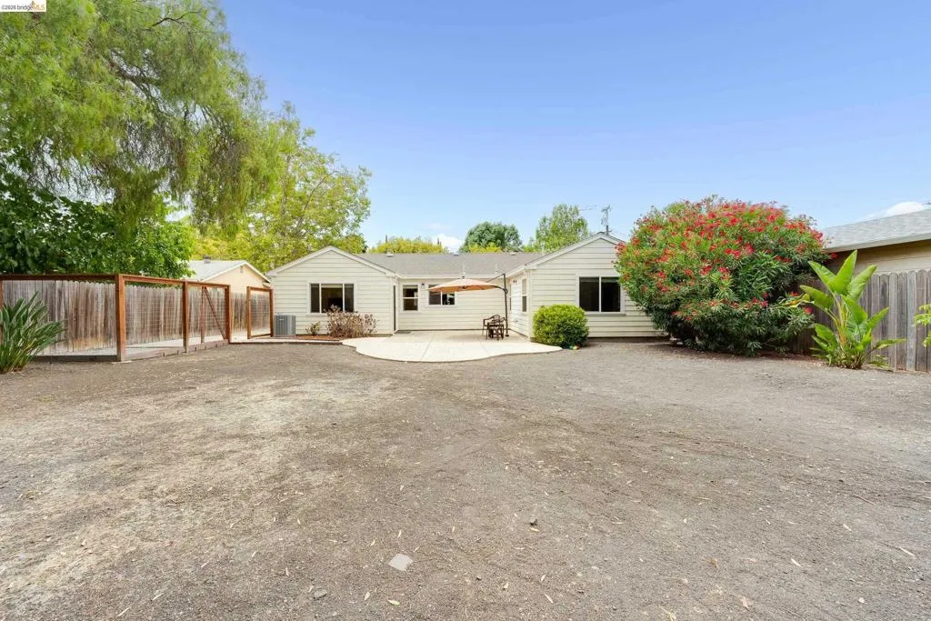 Expansive gravel yard featuring a large patio, mature trees, and a wooden fence