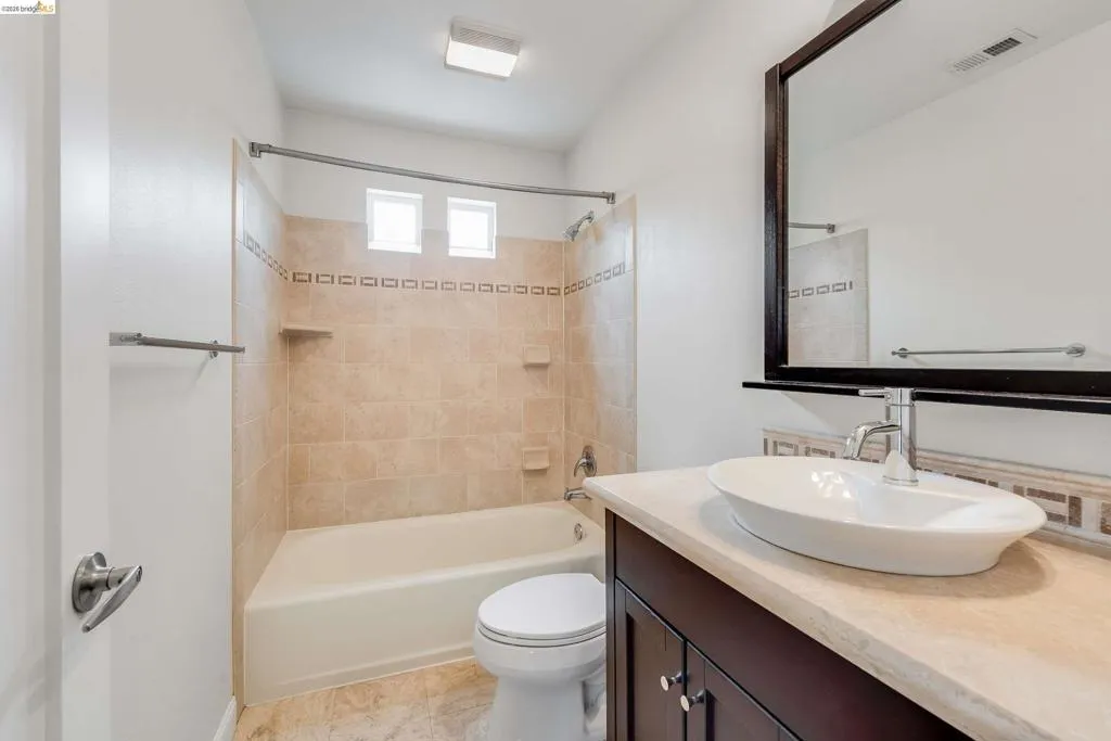 Bathroom featuring a vanity with an oval vessel sink, chrome faucet, and a stone-finish countertop