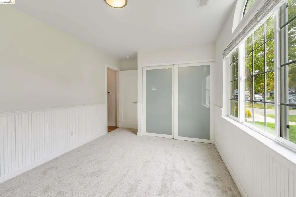 Room featuring a large window with gridded panes, light gray carpeting, beadboard wainscoting, and white walls
