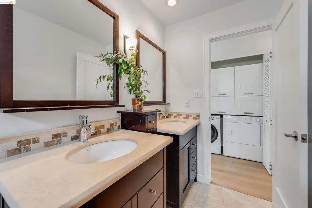 Dual sink vanity featuring dark wood-finish cabinetry, light-toned countertops, and a tiled backsplash
