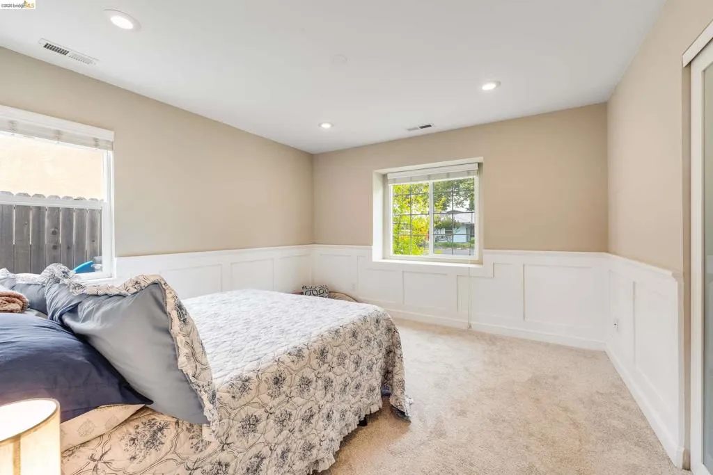 Bright room featuring two windows, recessed lighting, neutral wall paint, white wainscoting, and carpet flooring