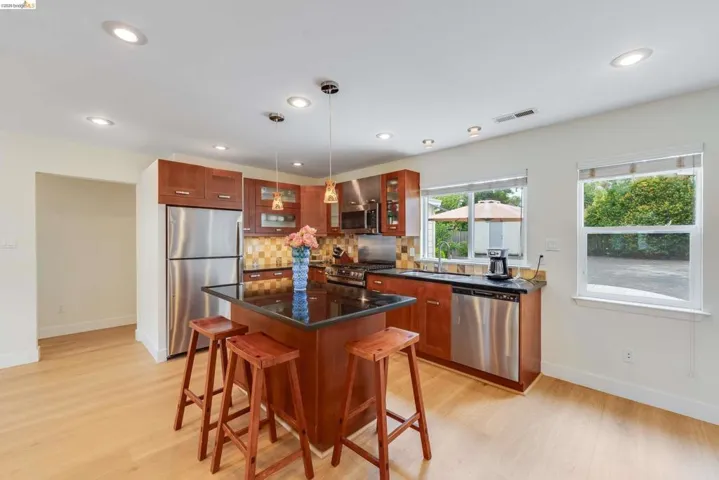 Kitchen featuring a central island with a dark countertop, stainless steel appliances, recessed lighting, wood-finish flooring, and multiple windows