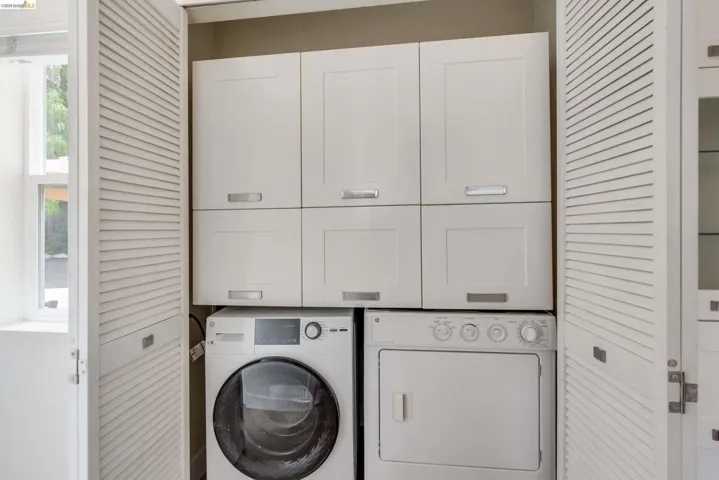 Integrated laundry area featuring a white front-load washer and dryer, upper cabinetry for storage, and white louvered bifold doors