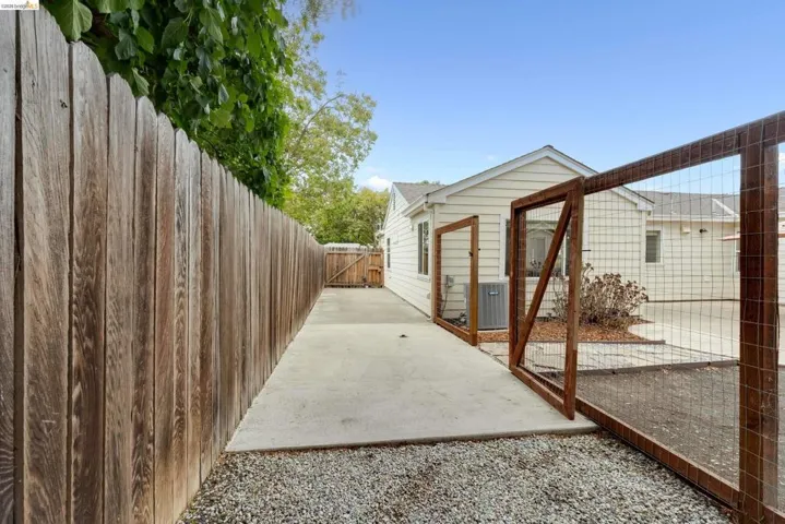 Concrete side yard with gravel bordering, wood privacy fencing, and a separate wood-framed wire fence enclosure