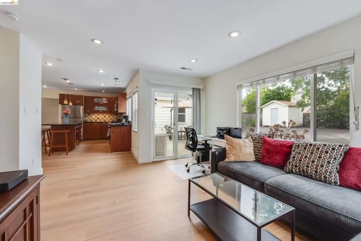 Spacious living area featuring light wood-finish flooring, recessed lighting, and a large window overlooking the backyard