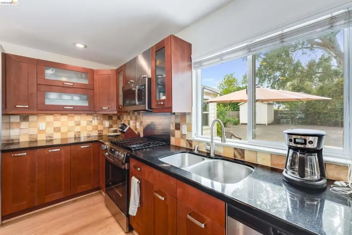Kitchen featuring wood-finish cabinetry, dark countertops, a checkerboard tile backsplash, and stainless steel appliances