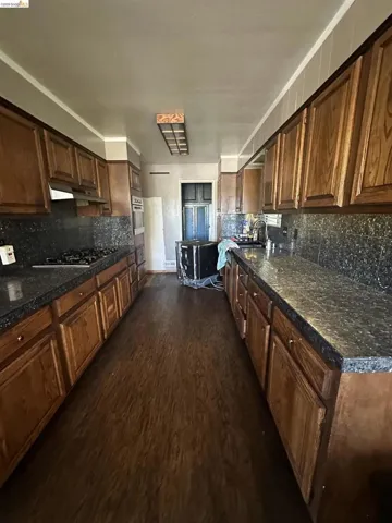 Galley kitchen featuring wood-finish flooring, wood cabinetry, dark speckled countertops, and a gas range