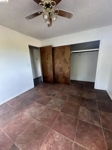 Spacious room featuring large format tile flooring, a ceiling fan with integrated lighting, and a double-door closet with wood-finish doors