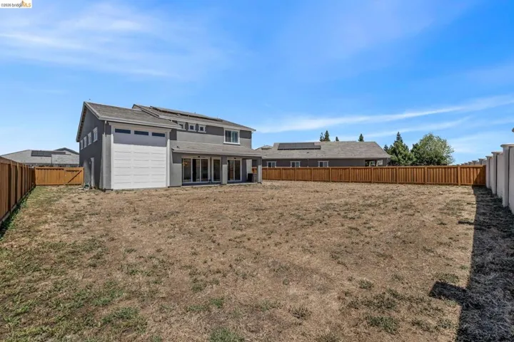 Expansive backyard featuring a new wooden fence, a concrete patio, and a two-story home with a gray stucco exterior
