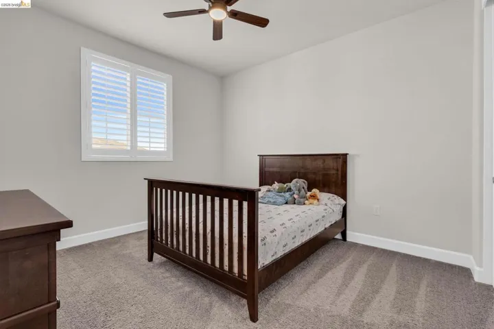 Room featuring light gray wall paint, gray carpeting, a window with plantation shutters, a ceiling fan with light fixture, and white baseboards