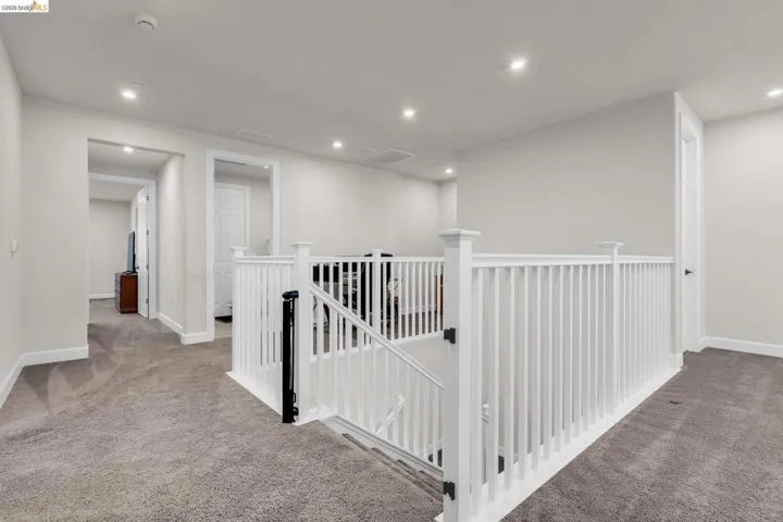 Upper-level landing featuring a white painted railing and neutral gray carpeting